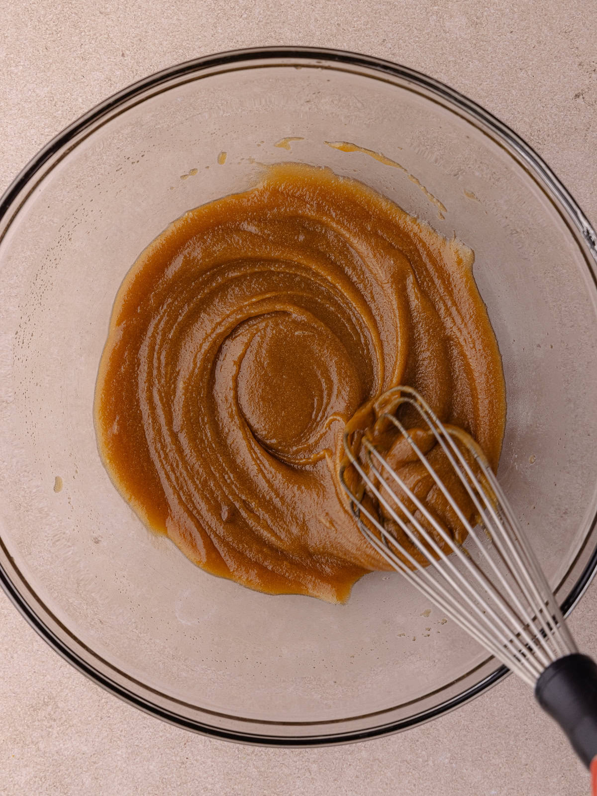 Melted butter and brown sugar are whisked in a large glass mixing bowl.