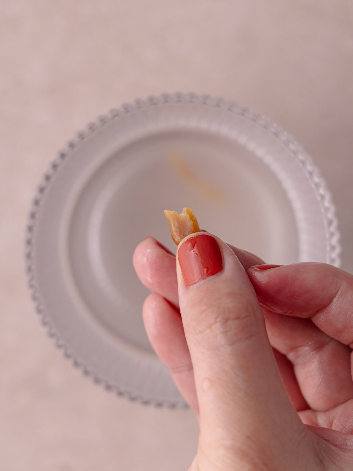 A hand holds a piece of toffee over a glass of cold water.