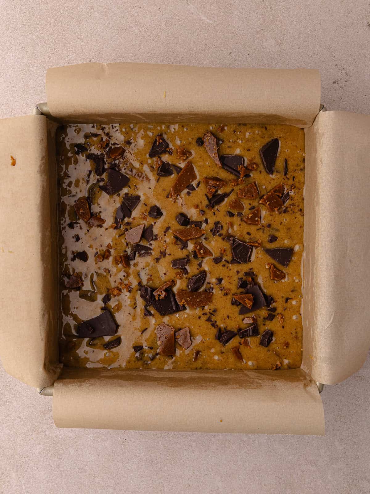 Toffee espresso blondies batter is transferred to a 8x8 inch pan that is lined with parchment paper.