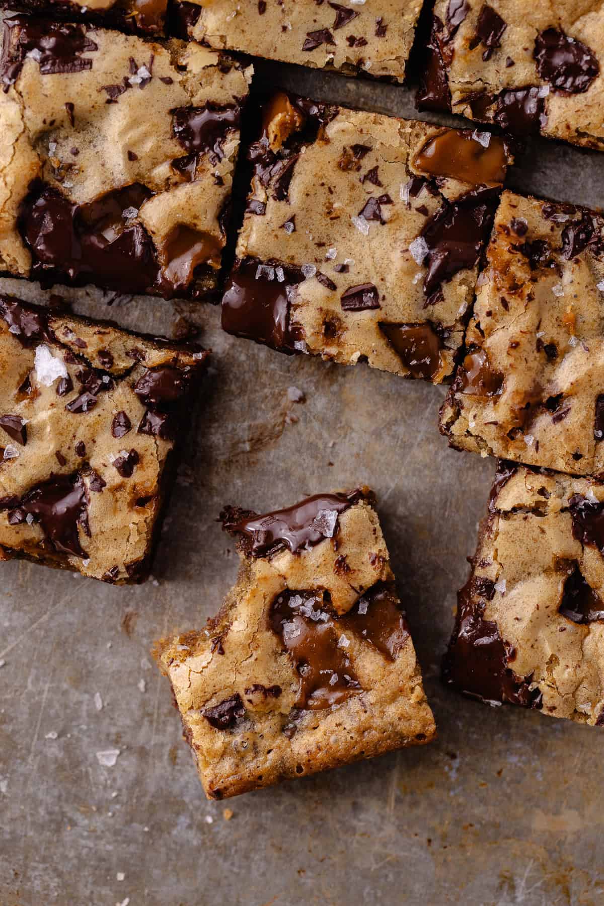 A close up of toffee espresso squares sitting on a baking sheet. A bite is taken out of one blondie square.