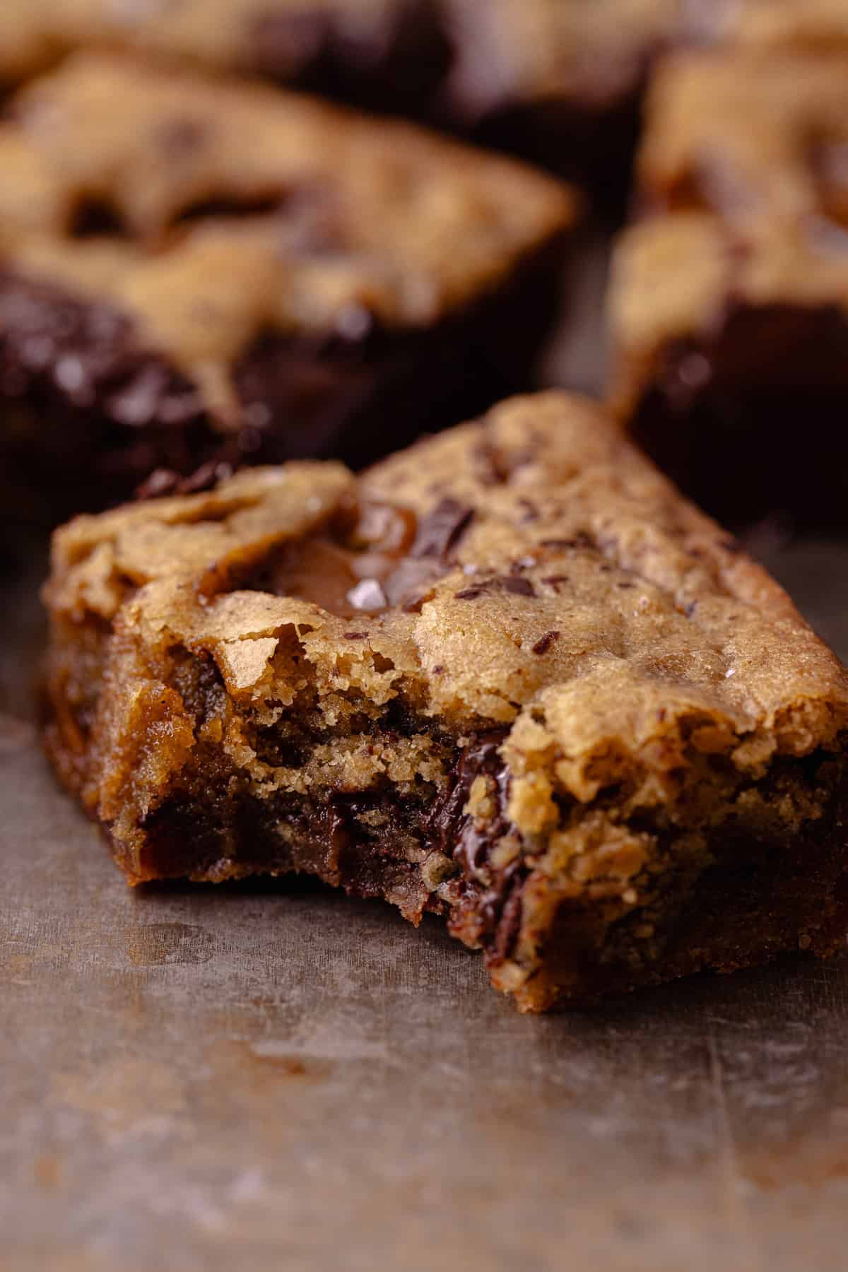 A close up of a salted toffee espresso blondie sitting on a baking sheet with a bite missing.