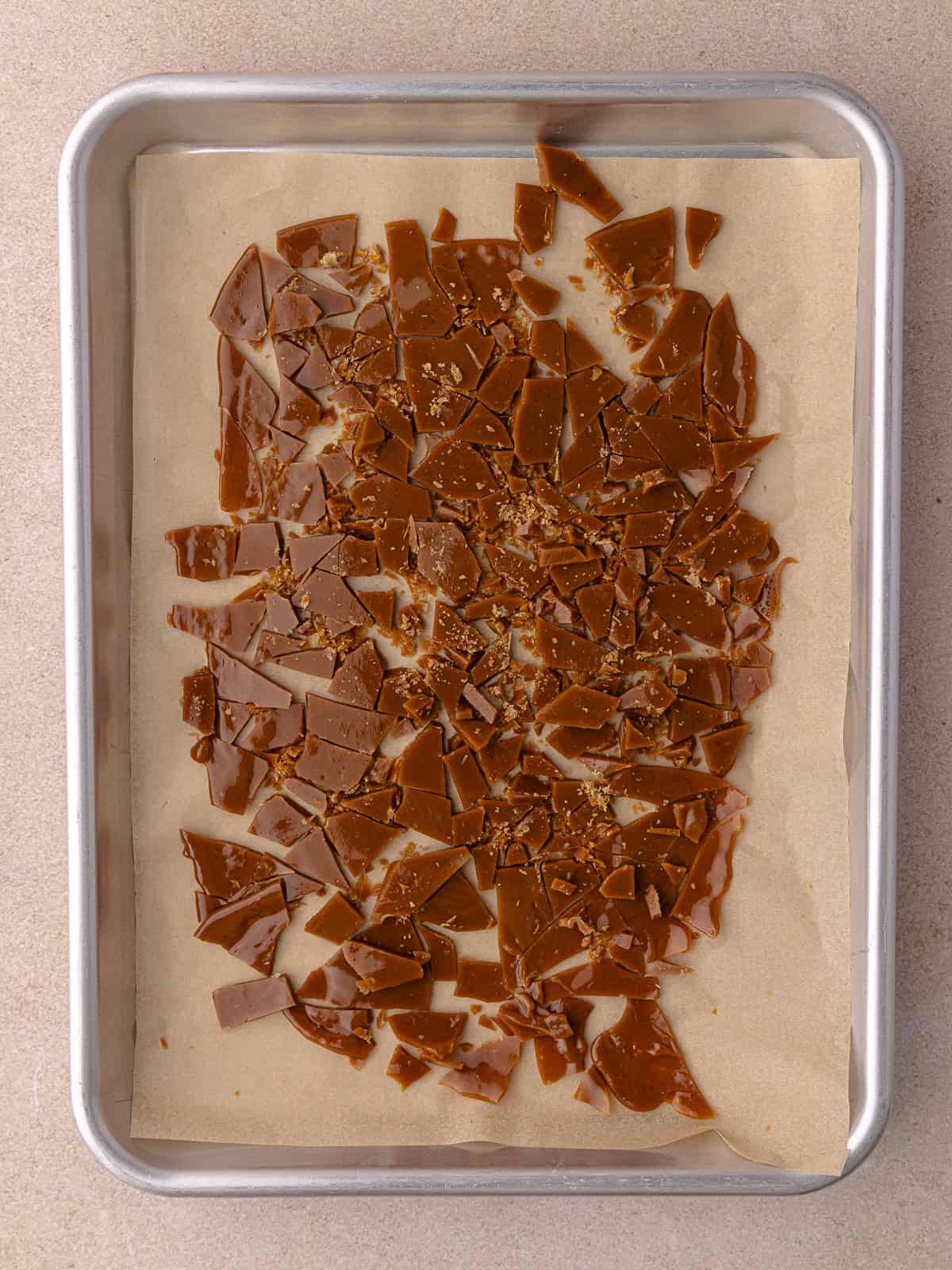 Homemade salted toffee bits are broken up into small pieces and are sitting on a small baking pan.