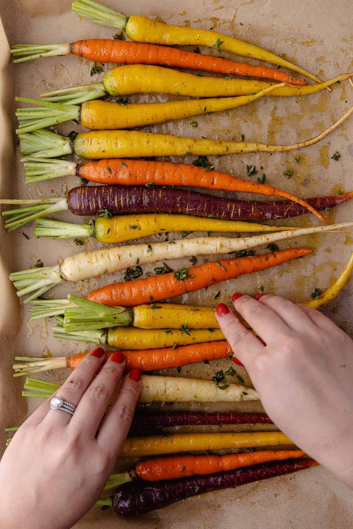 Rainbow carrots are on a baking sheet lined with parchment paper. The carrots are tossed in extra-virgin olive oil, fresh thyme, cumin, salt and black pepper.