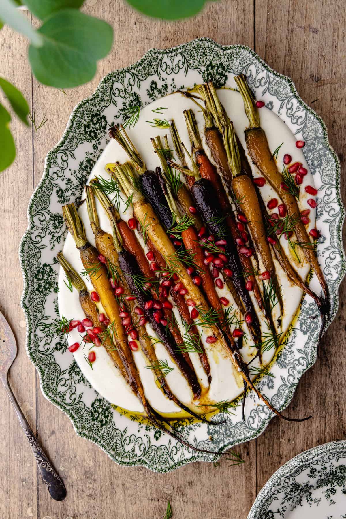 Garlic whipped feta with roasted cumin maple rainbow carrots on a large serving platter. It's garnished with pomegranate seeds and fresh dill.