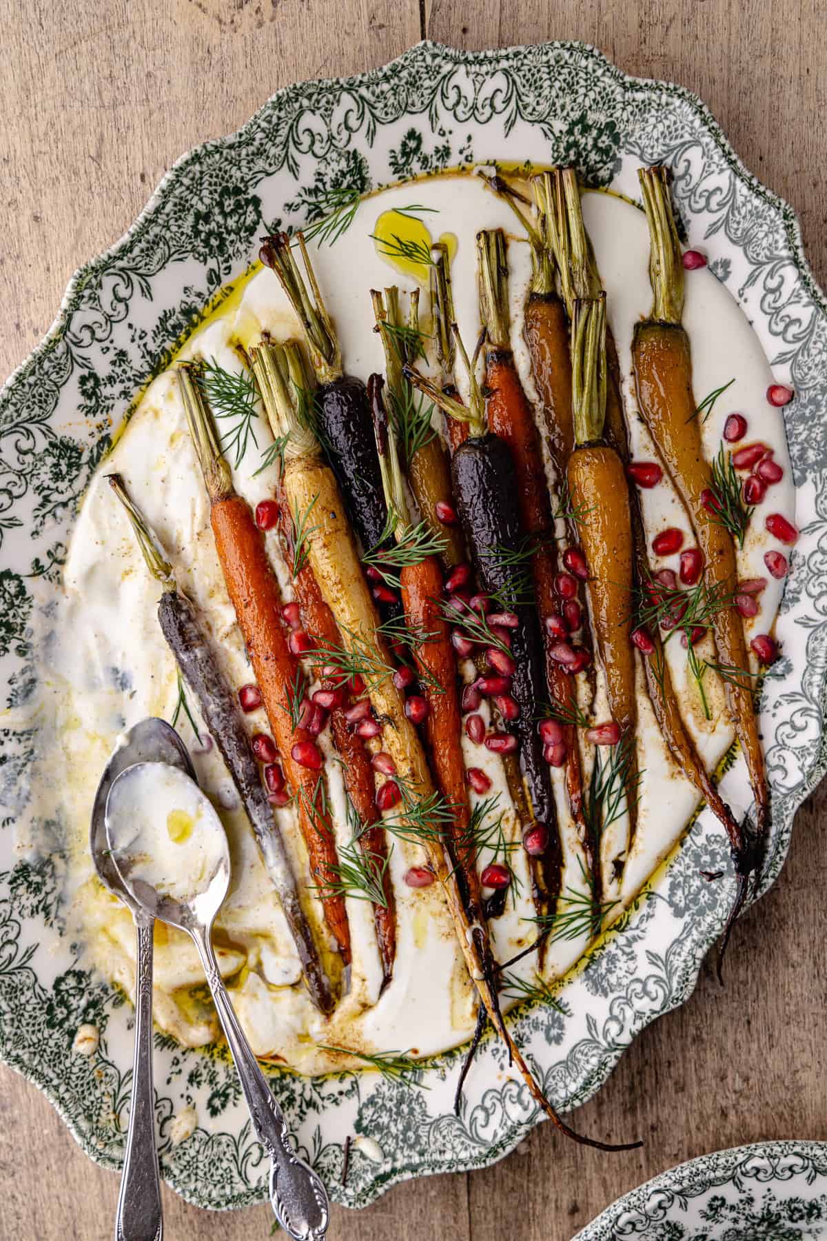 Garlic whipped feta with roasted cumin maple rainbow carrots on a large serving platter. It's garnished with pomegranate seeds and fresh dill.