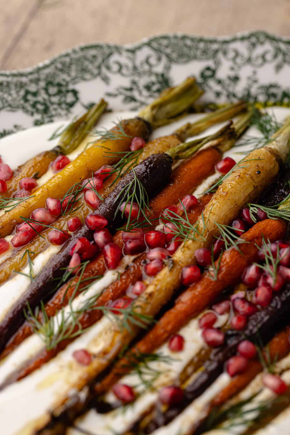 A close up of the garlic whipped feta with roasted cumin maple rainbow carrots on a large serving platter. It's garnished with pomegranate seeds and fresh dill.