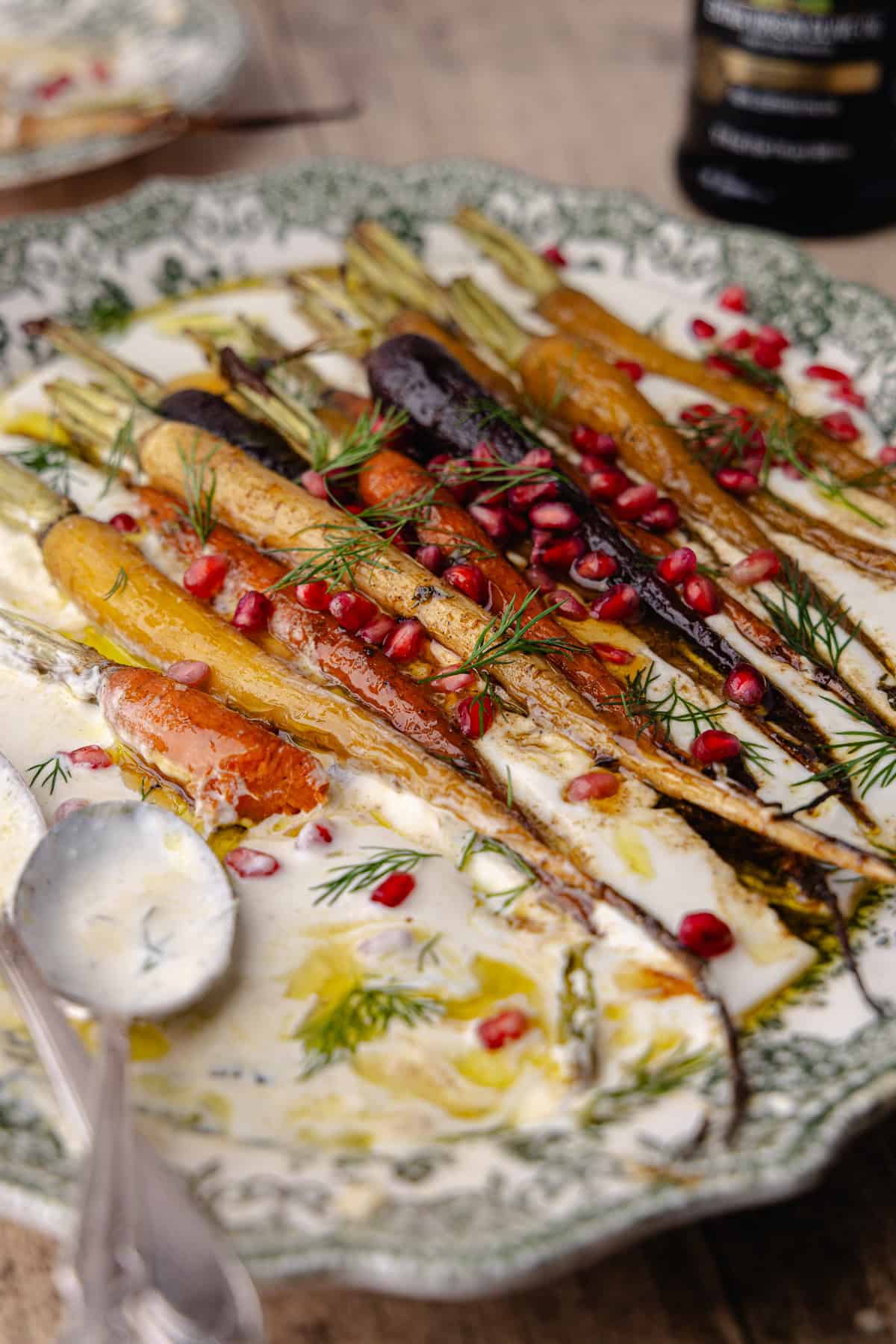 Garlic whipped feta with roasted cumin maple rainbow carrots on a large serving platter. It's garnished with pomegranate seeds and fresh dill.