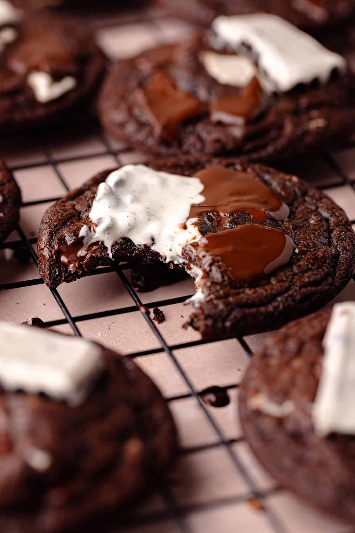 Chocolate cookies and cream cookies sitting on a wire rack with a bite missing.