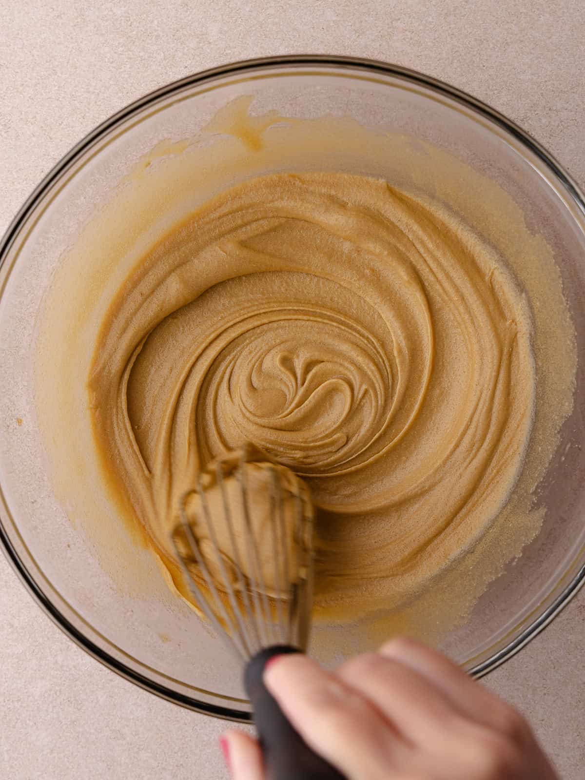 Egg and vanilla are whisked together in a large glass mixing bowl.