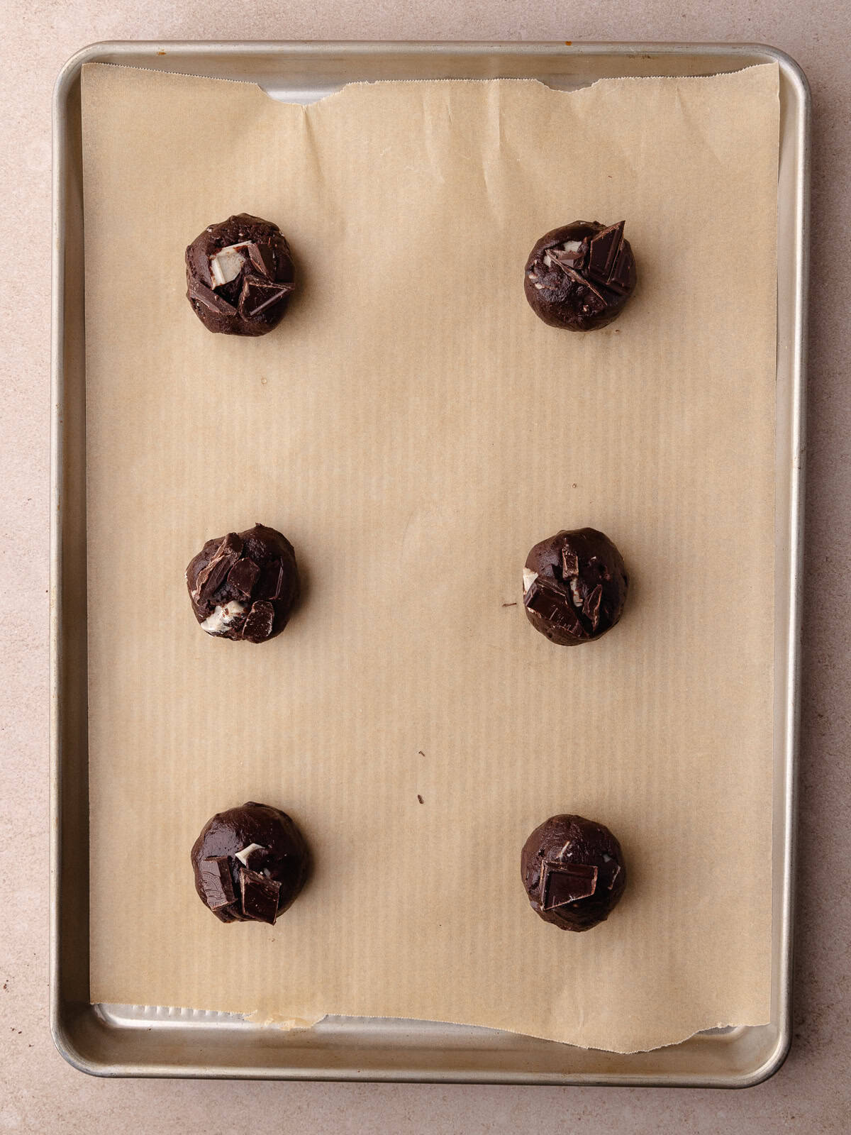 Six Chocolate cookies and cream cookies dough balls are sitting on a baking sheet and ready to be baked.