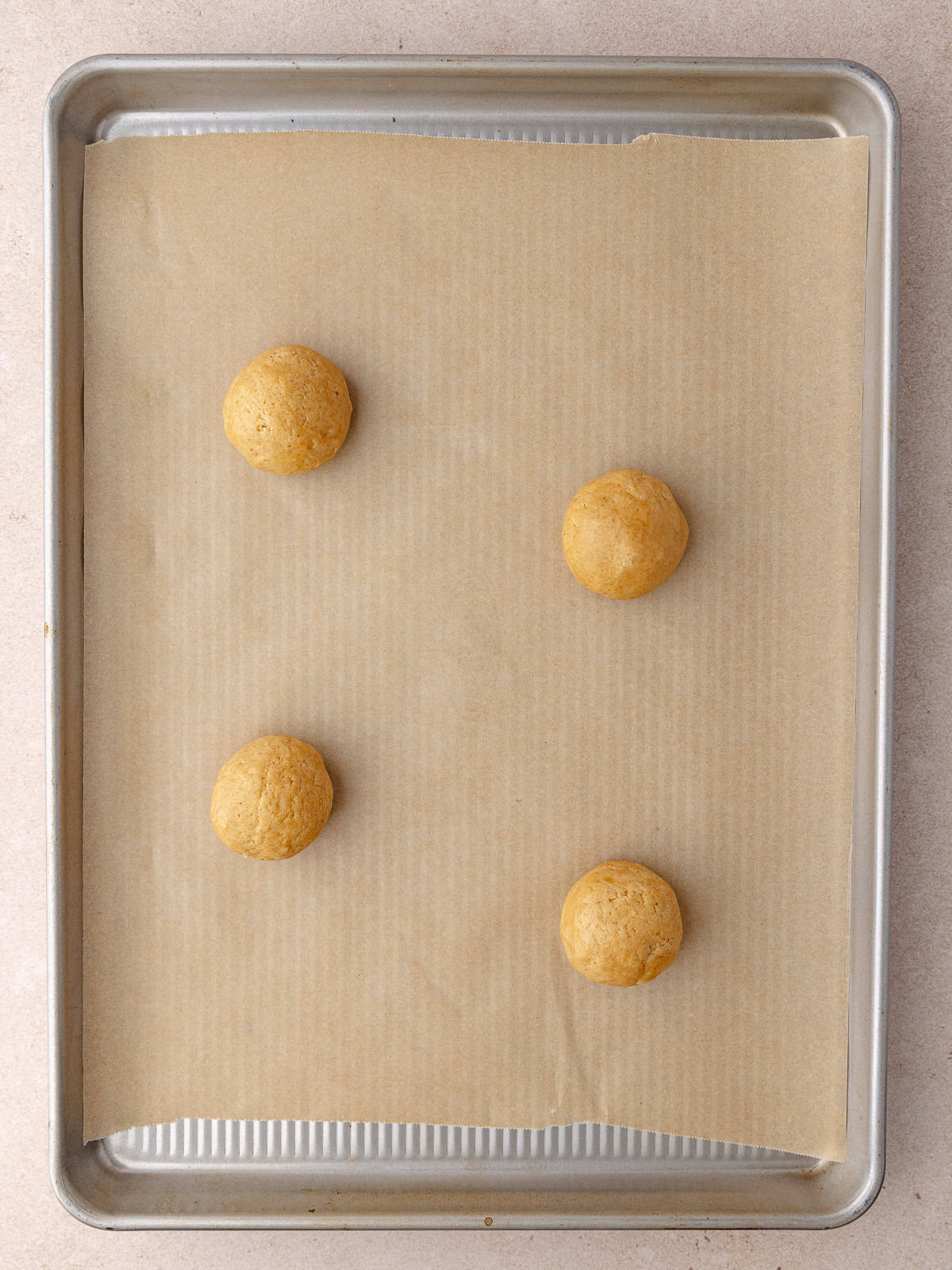 Raw cookie dough balls are on a baking sheet lined with parchment paper.