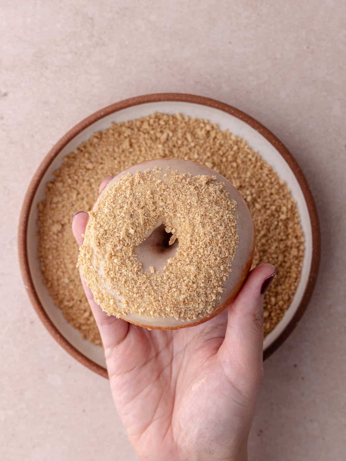 A glazed donut is dipped into a bowl of cinnamon toast crunch cereal crumbs.