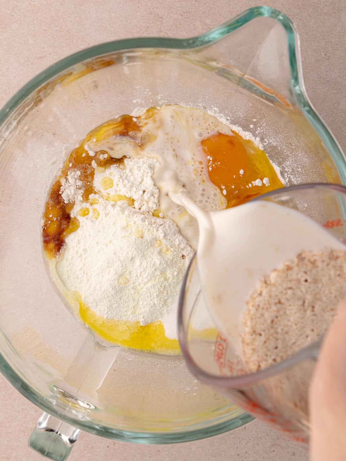 Bloomed yeast mixture is poured into a large stand mixer bowl with bread flour, all-purpose flour, dry milk powder, sugar, dry milk powder, egg, yolk, vanilla, cinnamon and salt