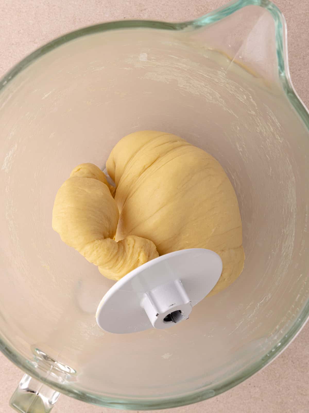 Cinnamon toast crunch donut dough is done kneading and his sitting in a large glass bowl with a dough hook attached.