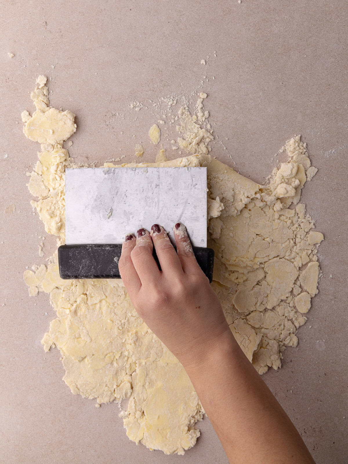 A bench scraper folds the flattened dough over it self.