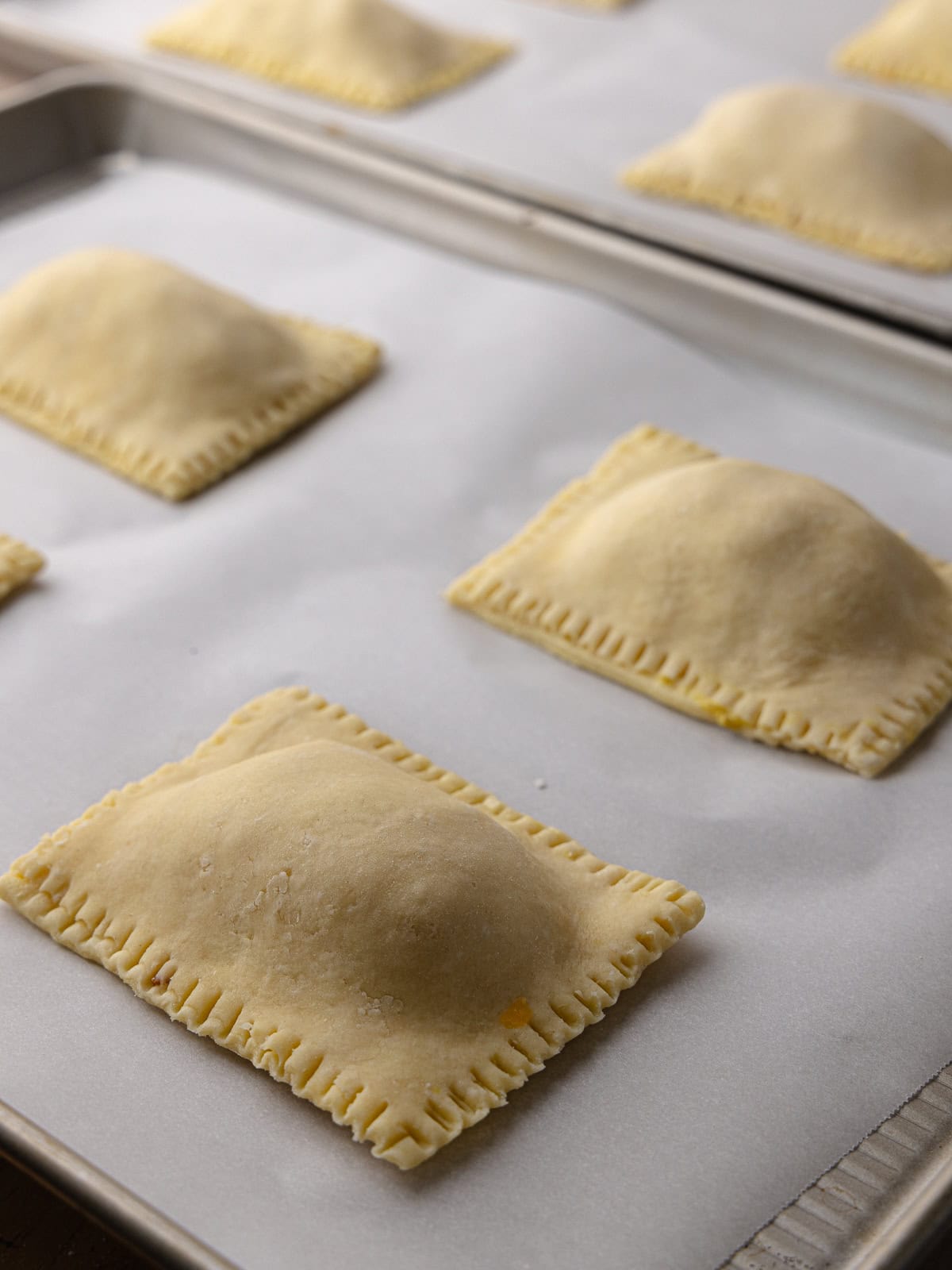 Super flaky and tender ham and cheese hand pies are filled and sitting on baking sheets.