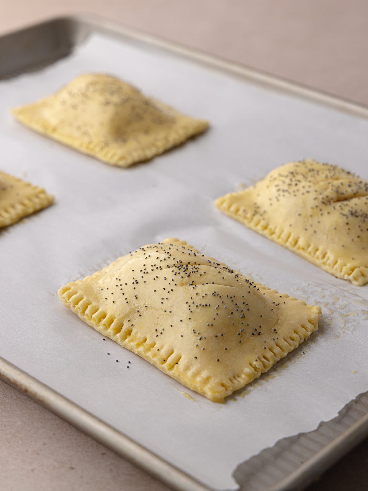 Super flaky and tender ham and cheese hand pies sitting on baking sheet waiting to be baked.