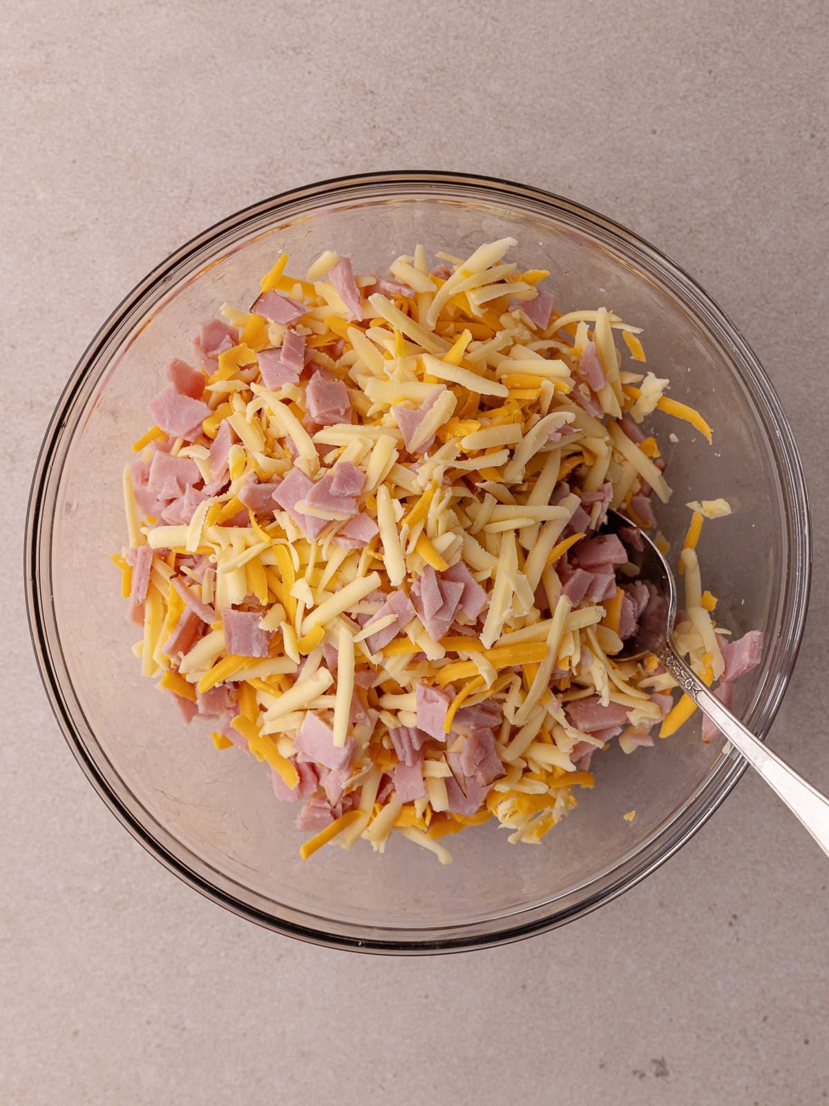 Chopped black forest ham, shredded gouda cheese and sharp cheddar cheese are mixed together in a medium glass bowl.