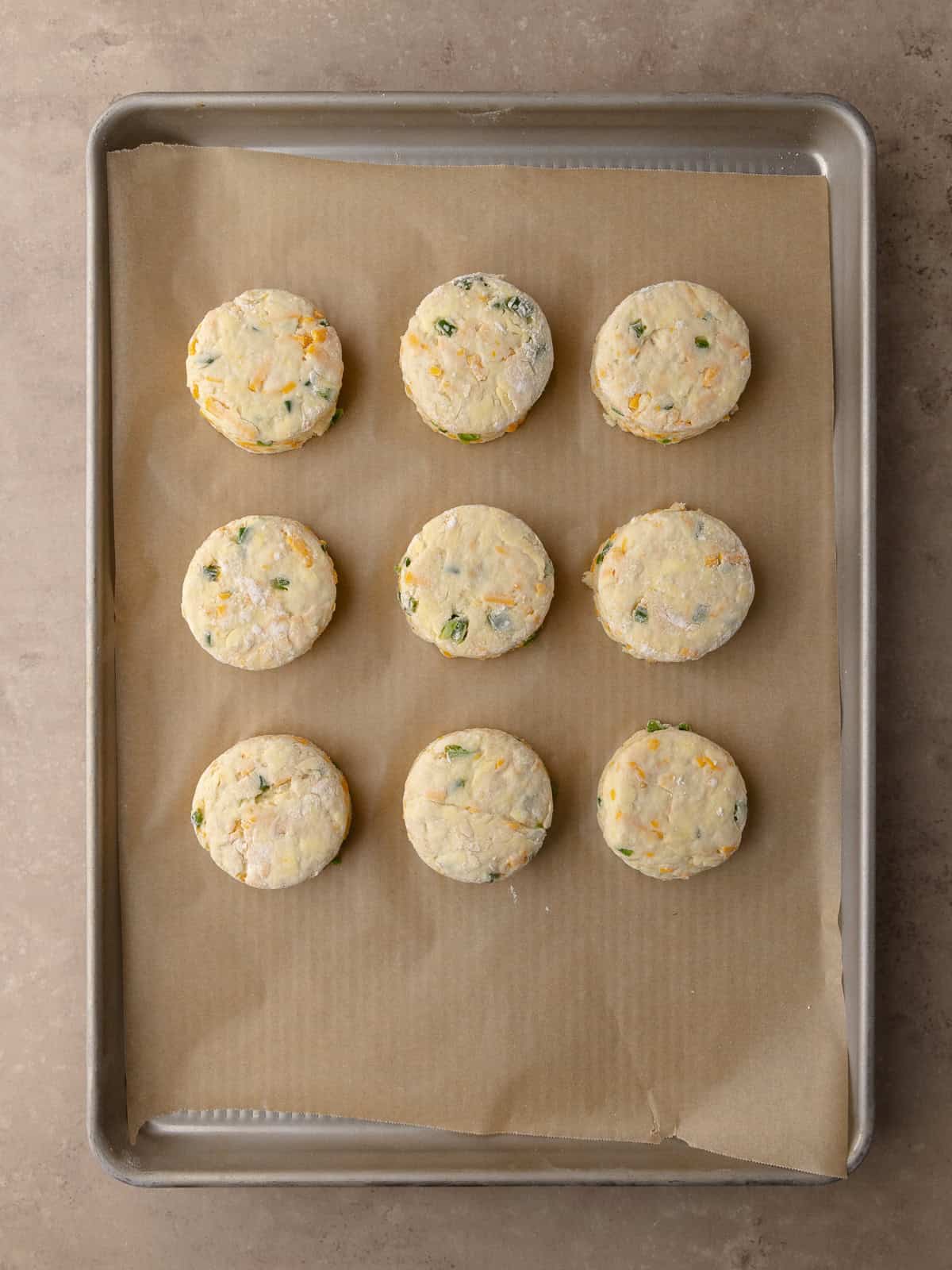 Cut out Buttermilk Jalapeño cheddar biscuits sitting on a baking tray lined with parchment paper.