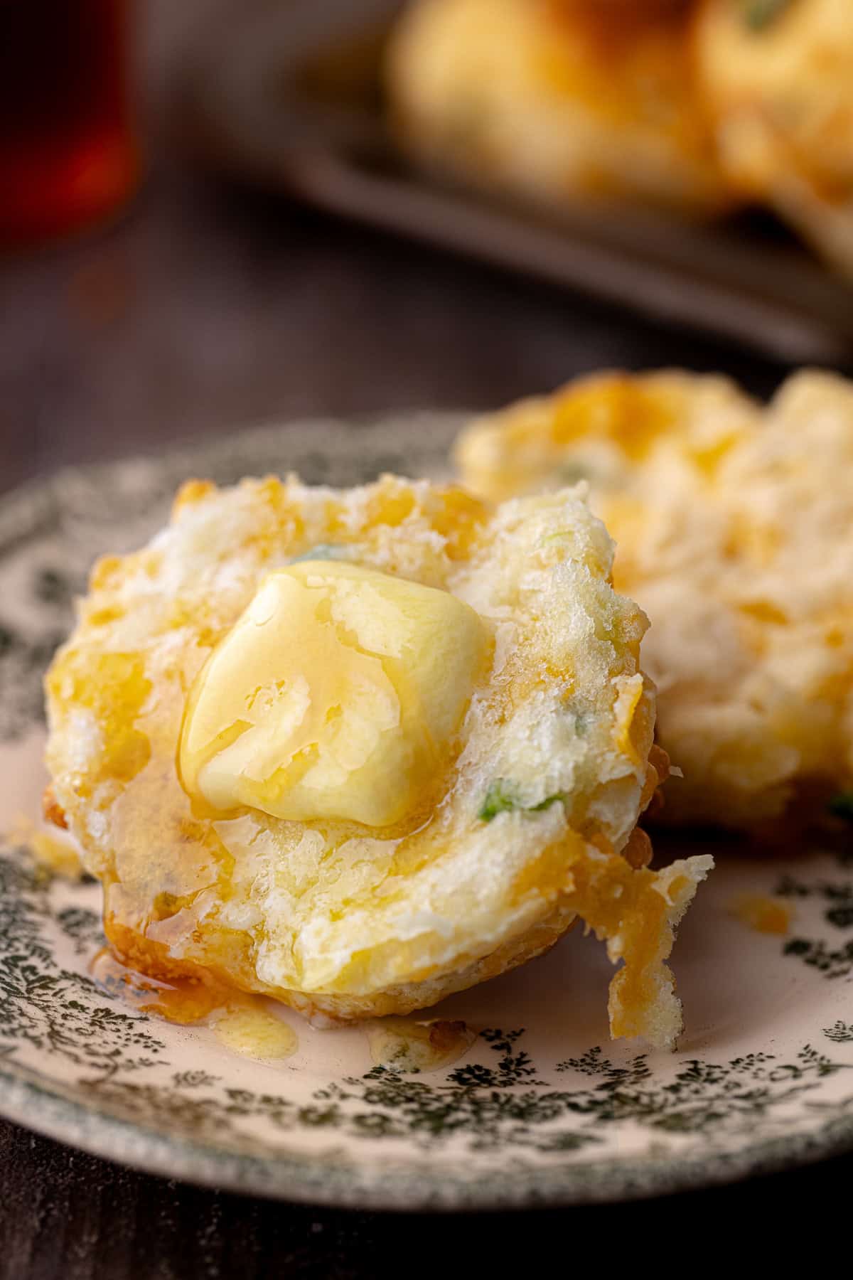 Tall flaky buttermilk Jalapeño cheddar biscuit sitting on a small plate with butter and hot honey.