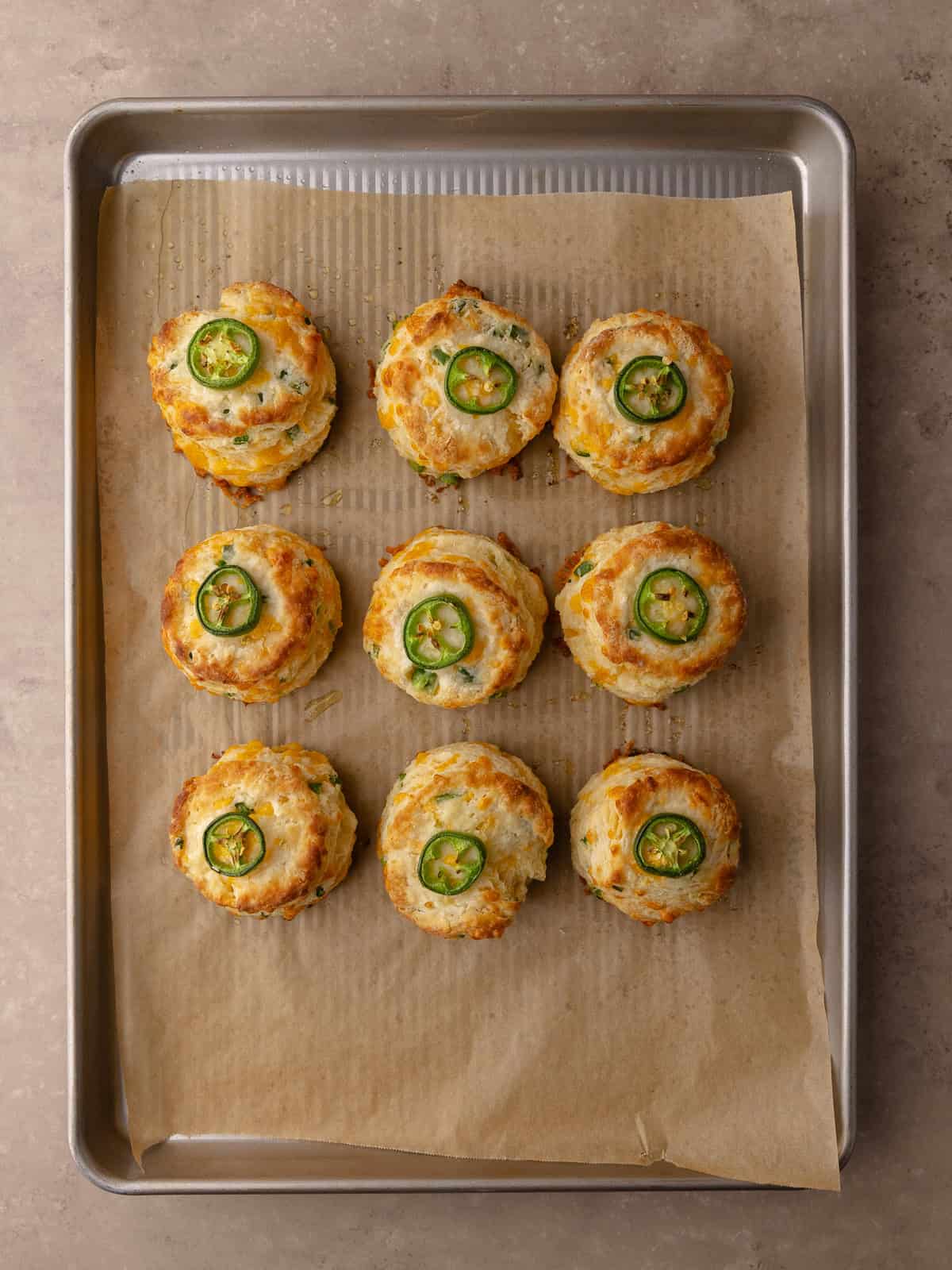 Tall and flaky Buttermilk Jalapeño cheddar biscuits are baked until golden brown and sitting on a baking sheet.