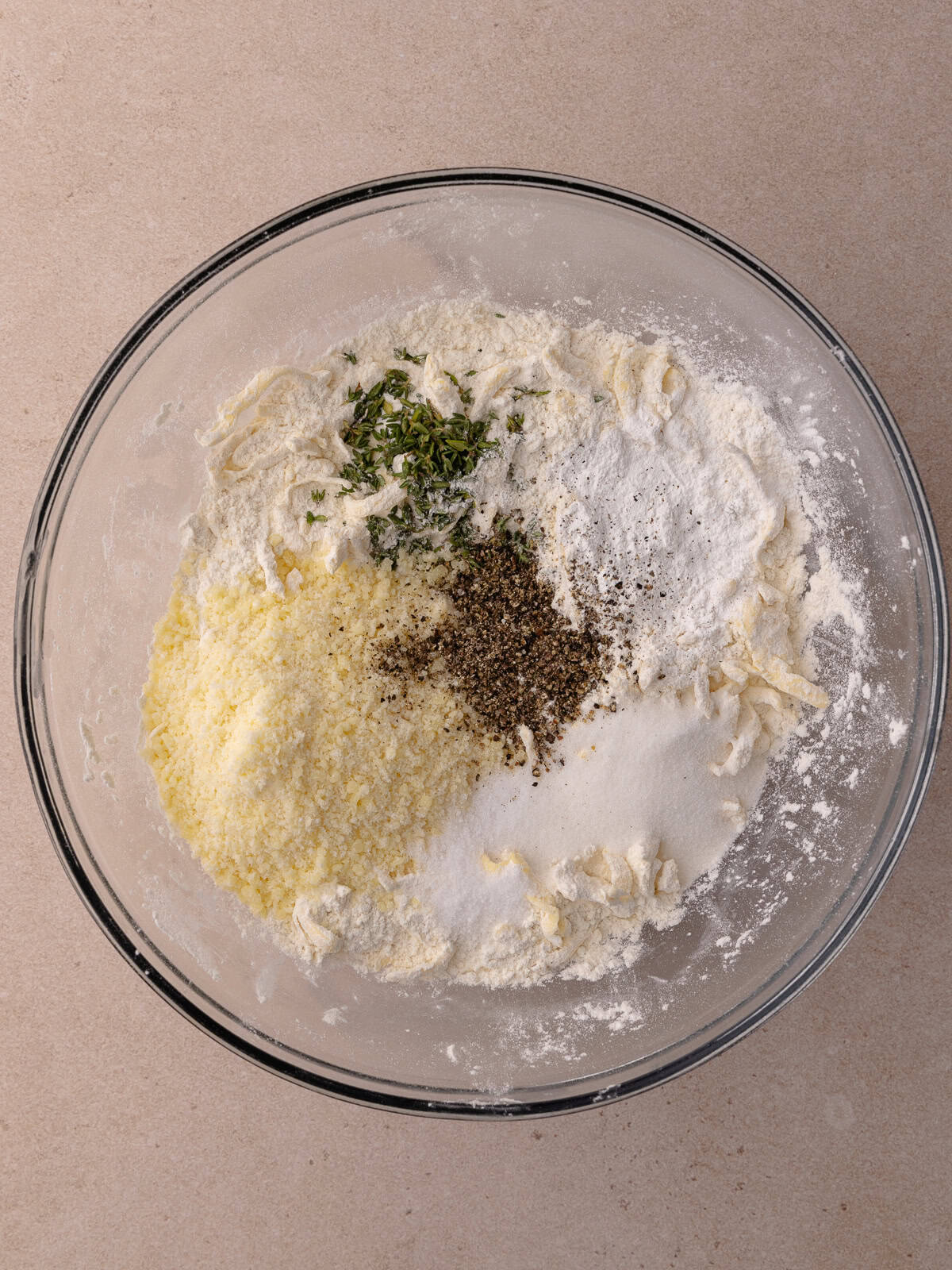 Grated parmesan, fresh thyme, sugar, salt, black pepper, baking powder are added to the bowl with the flours and grated butter.