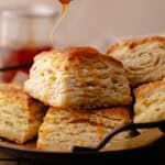 Hot honey drizzled over tall and flaky Parmesan Black Pepper Thyme Biscuits sitting a serving plate feature photo.