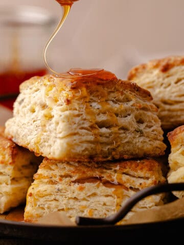 Hot honey drizzled over tall and flaky Parmesan Black Pepper Thyme Biscuits sitting a serving plate feature photo.