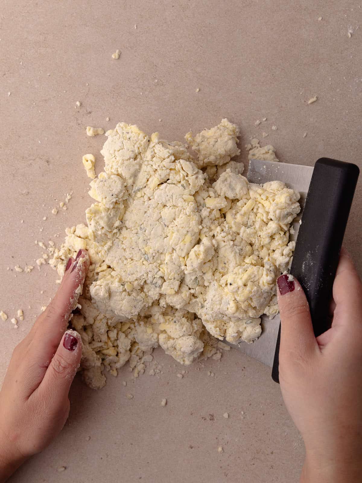 The shaggy thyme biscuit dough is gathered together with a bench scraper.