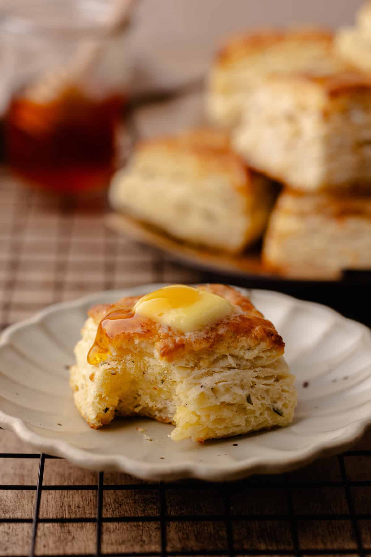 Tall and flaky Parmesan Black Pepper Thyme Biscuits sitting on small plate topped with butter and hot honey.