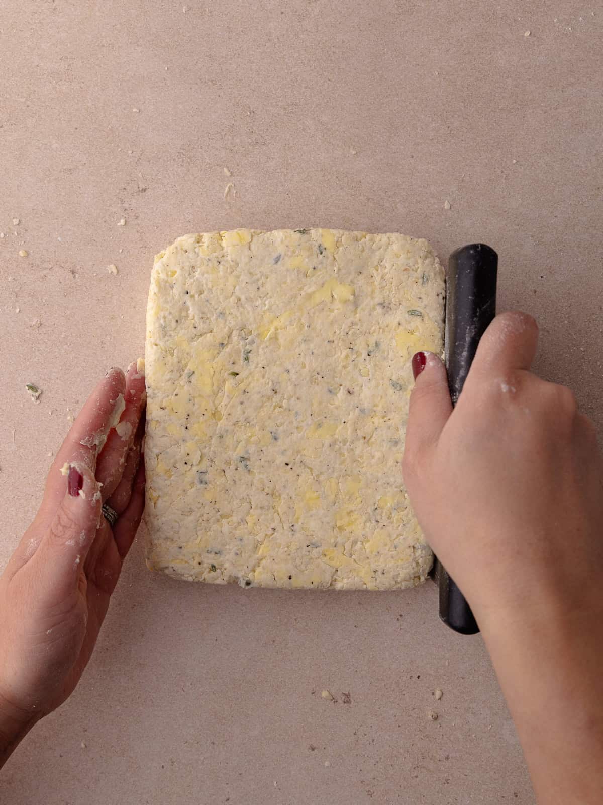 Thyme biscuit dough is rolled our one final time and shaped into a square with a bench scraper.