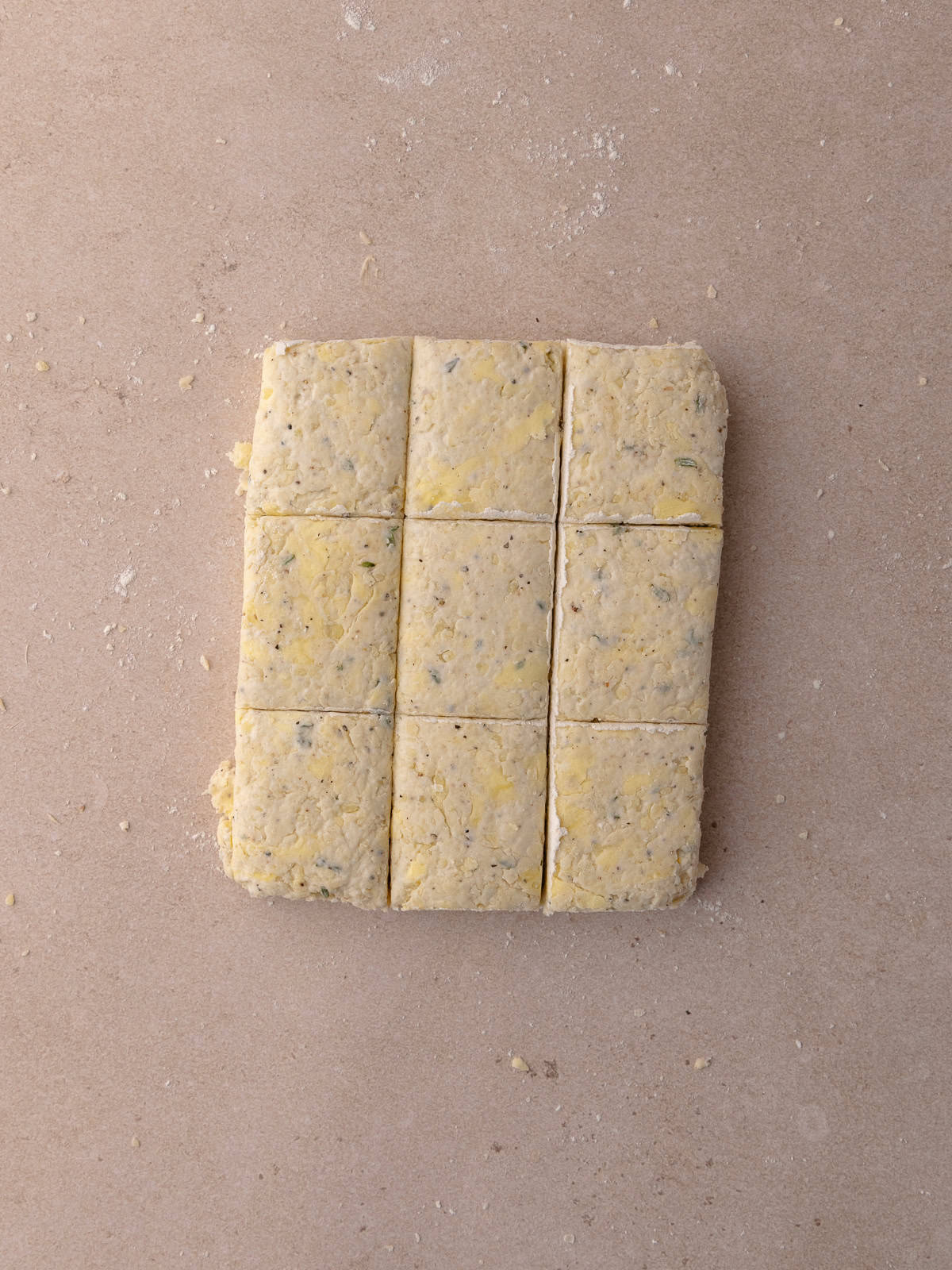 The parmesan black pepper thyme biscuit dough is trimmed on the edges and then cut into 9 squares.