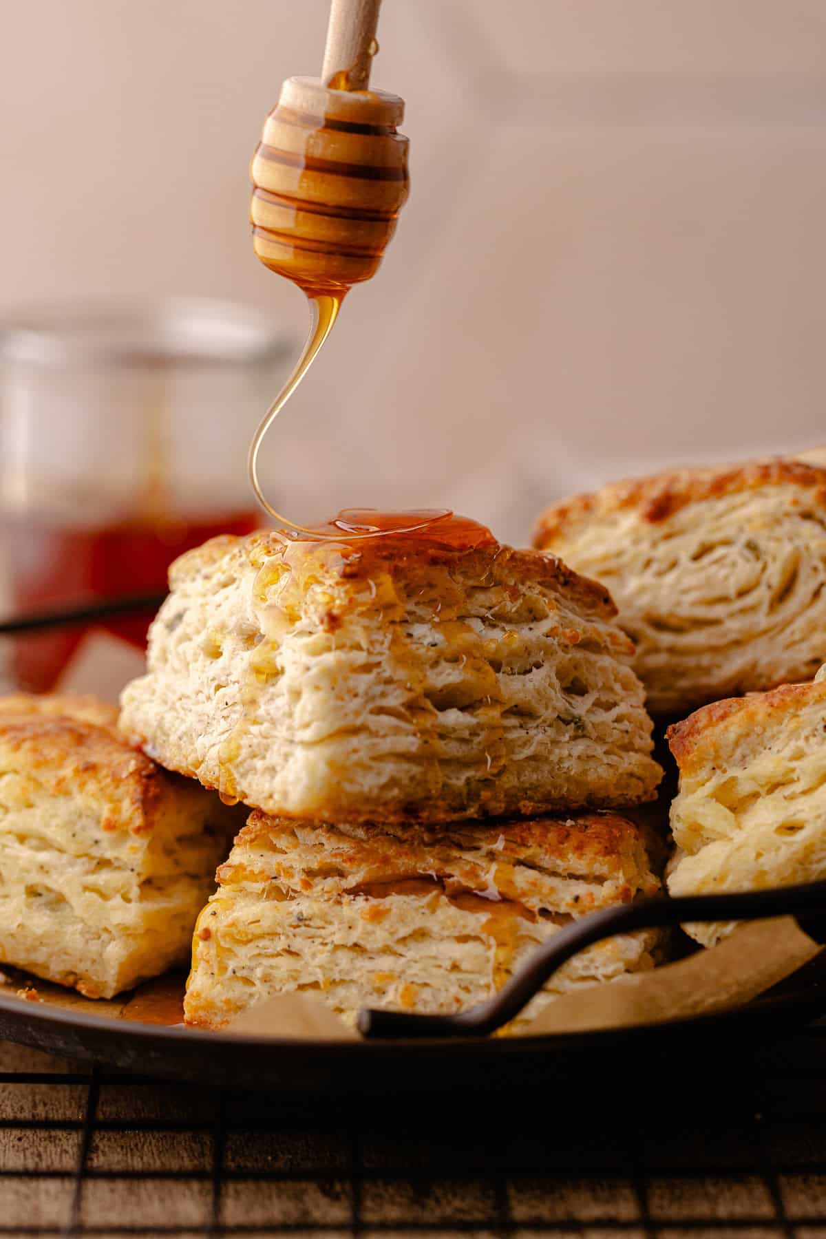 Tall and flaky Parmesan Black Pepper Thyme Biscuits sitting on a serving tray drizzled with hot honey.