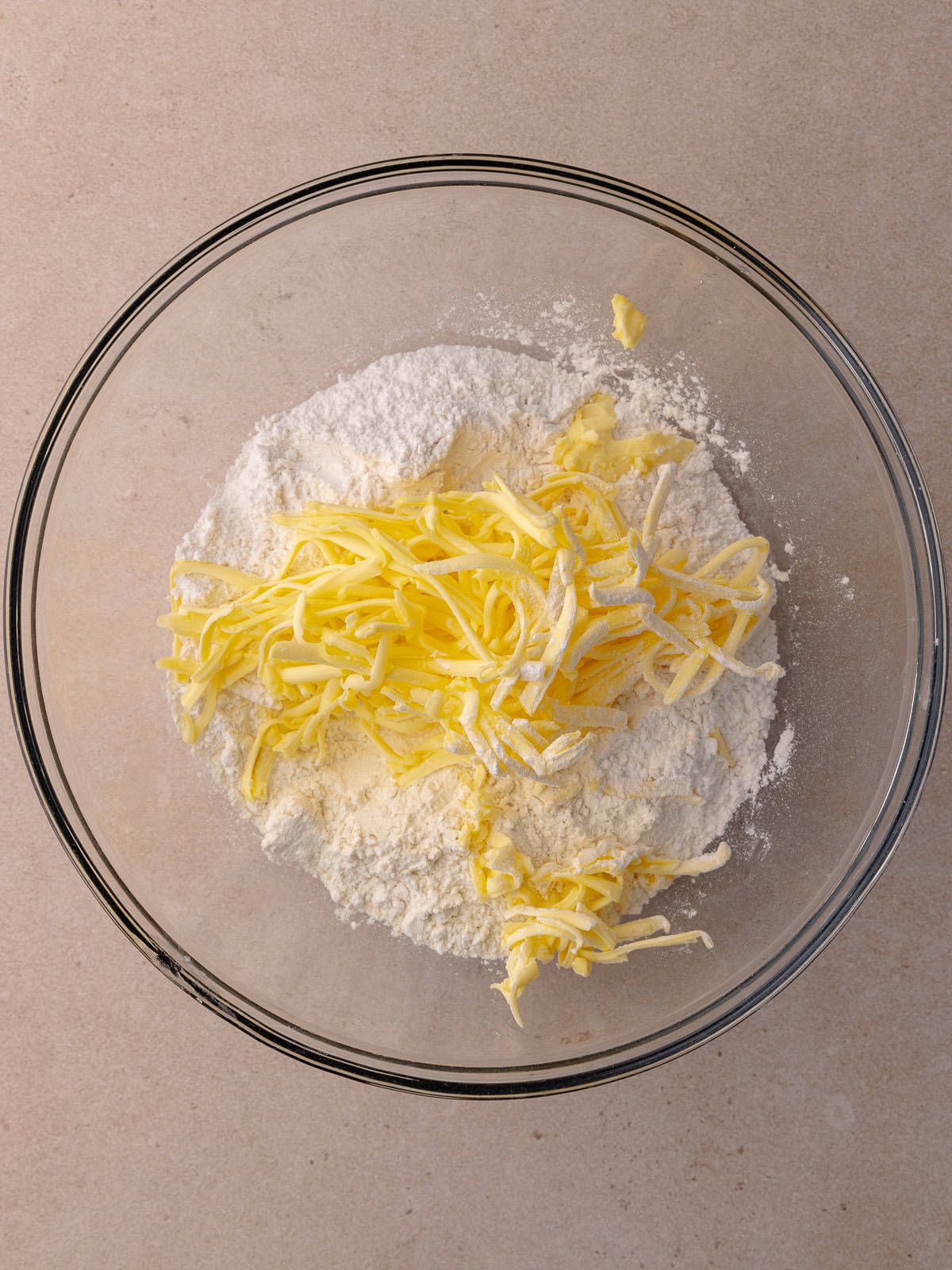 All-purpose flour, cake flour and shredded butter are sitting in a large glass mixing bowl.