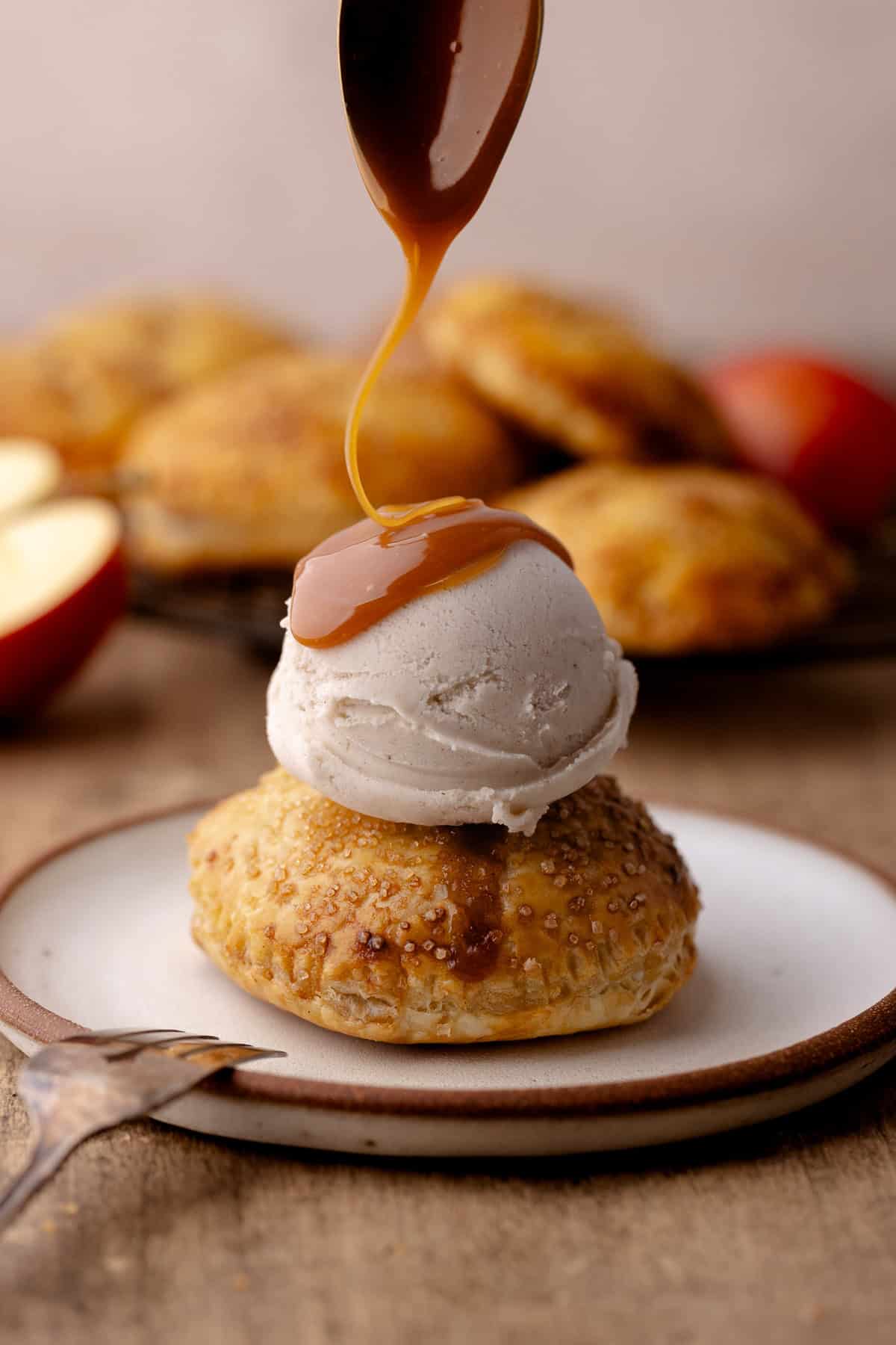 Puff pastry apple hand pie on a plate with a scoop of ice cream and caramel sauce drizzled over the top.