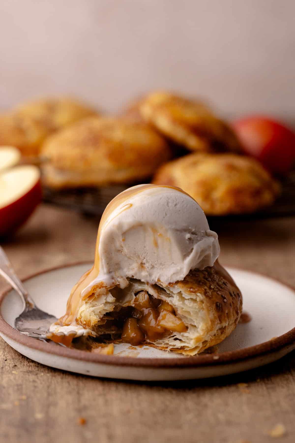 Puff pastry apple hand pie on a plate with a scoop of ice cream and caramel sauce.