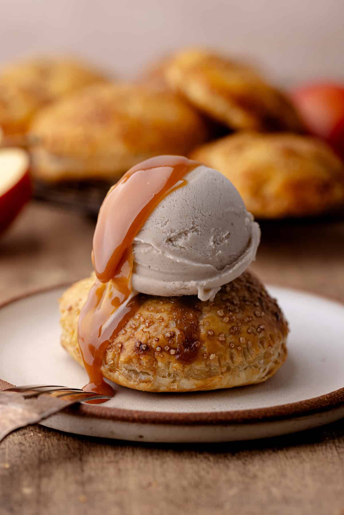 Puff pastry apple hand pie topped with a scoop of ice cream and salted caramel drizzle sitting on a plate.