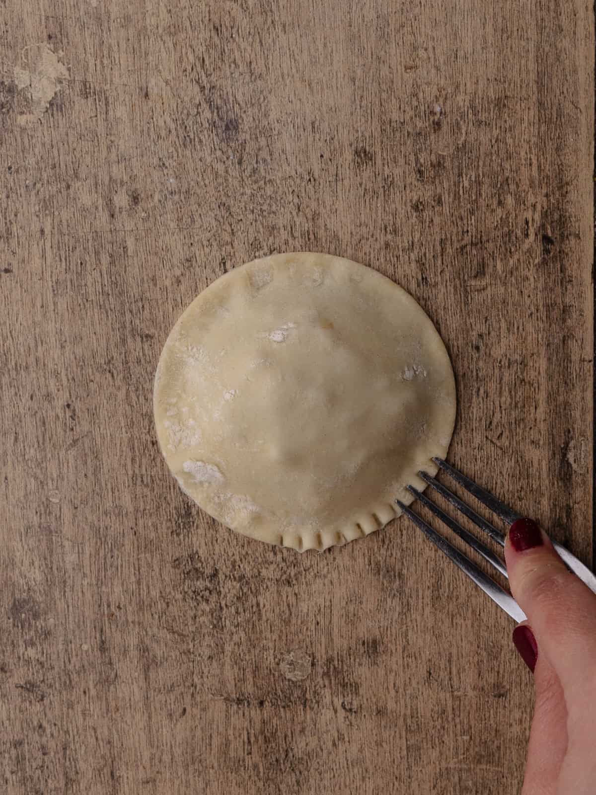 Puff pastry apple hand pie is crimped with a fork to seal the edges.