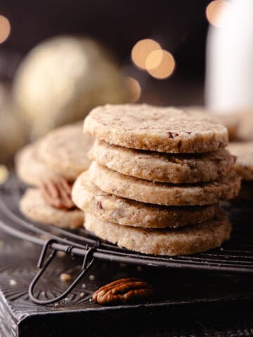 Brown butter pecan cookies with maple and cinnamon, stacked and sitting on a wire rack feature photo.