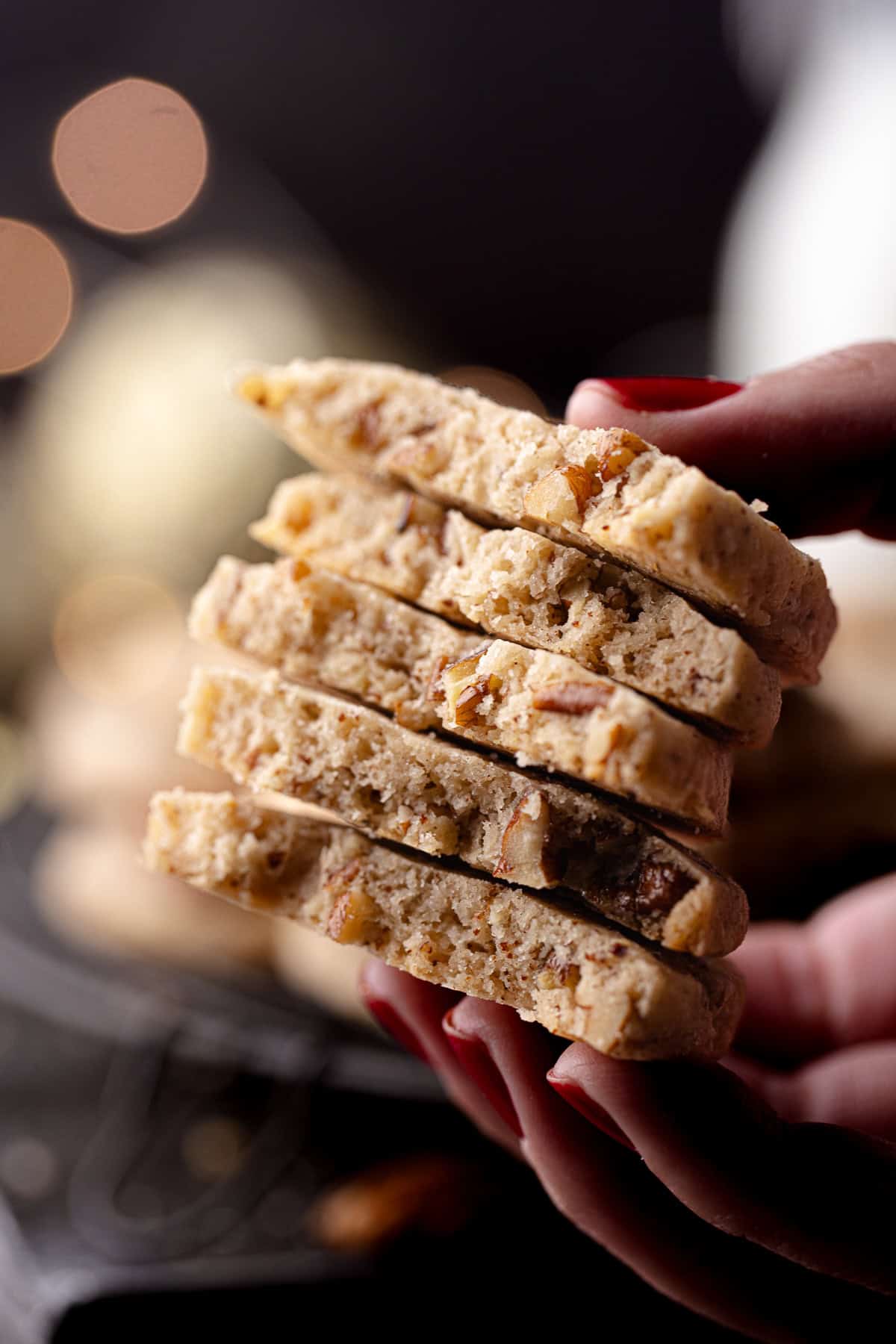 A close up of a hand holding a stack of brown butter pecan cookies with maple and cinnamon.