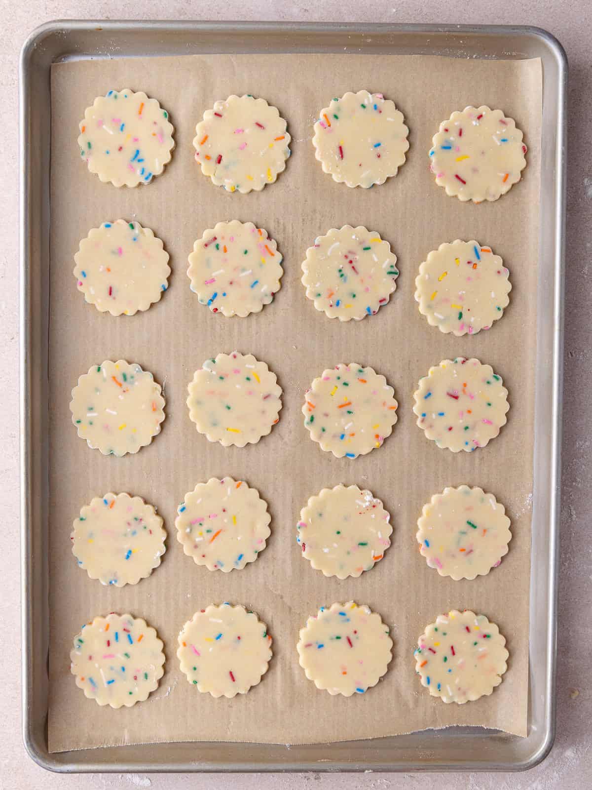 Funfetti shortbread cookies are stamped out and sitting on a large baking sheet.