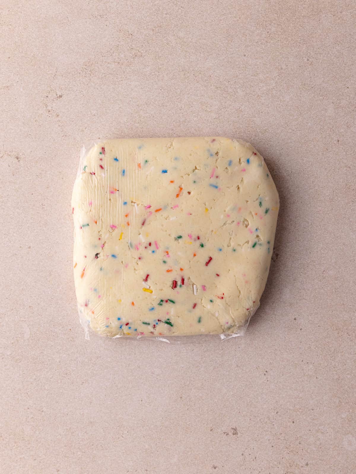 Funfetti shortbread cookie dough is wrapped in plastic wrap.