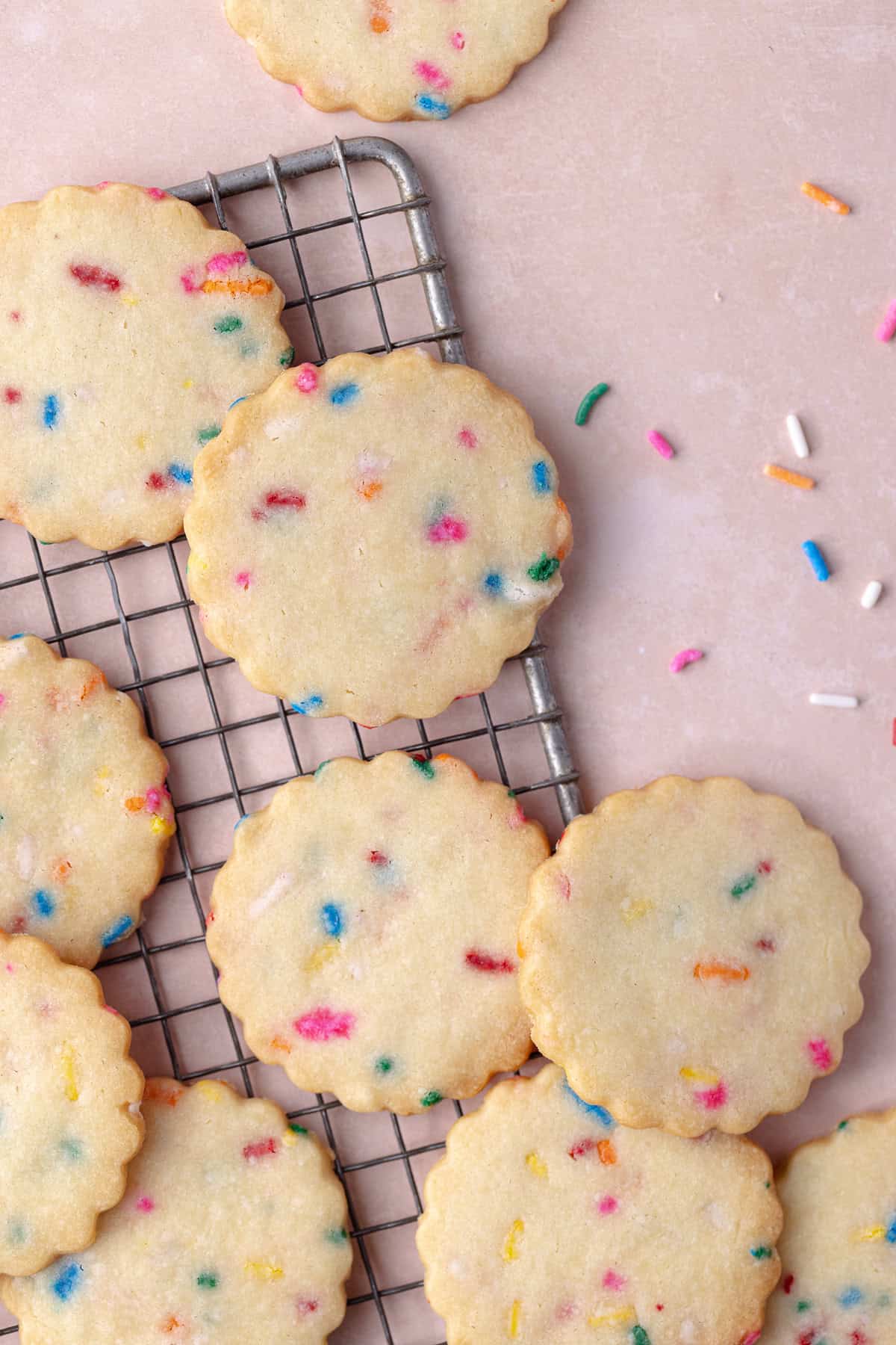 Funfetti shortbread cookies are scattered on a small wire rack with rainbow sprinkles.