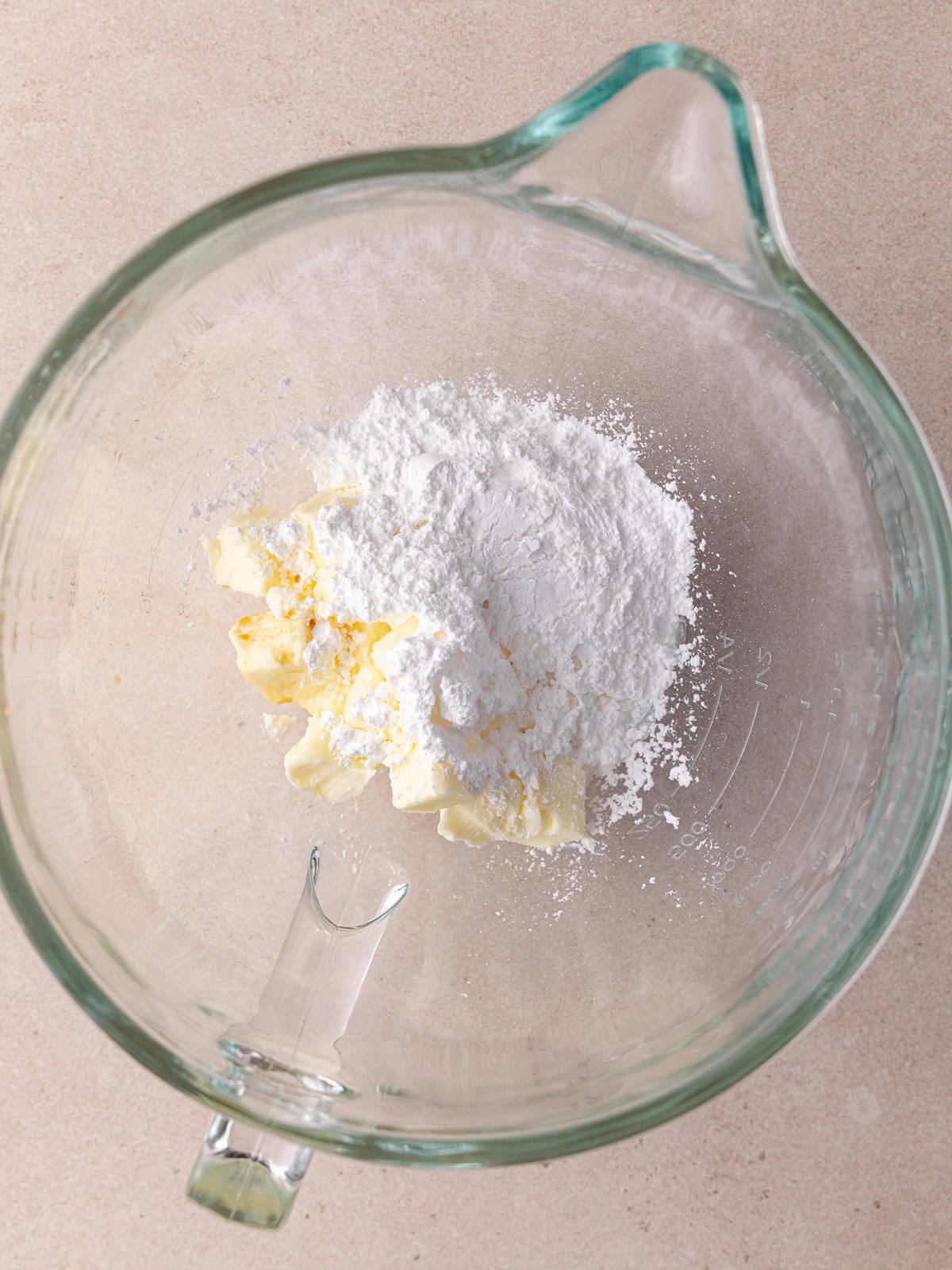 Softened butter, powdered sugar, almond extract and vanilla extract are in a large glass mixing bowl.