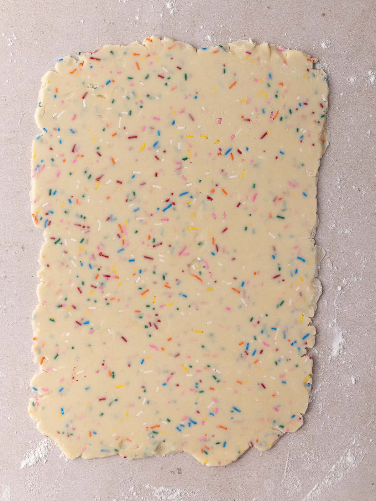 Funfetti shortbread cookie dough is rolled out on a floured work surface.