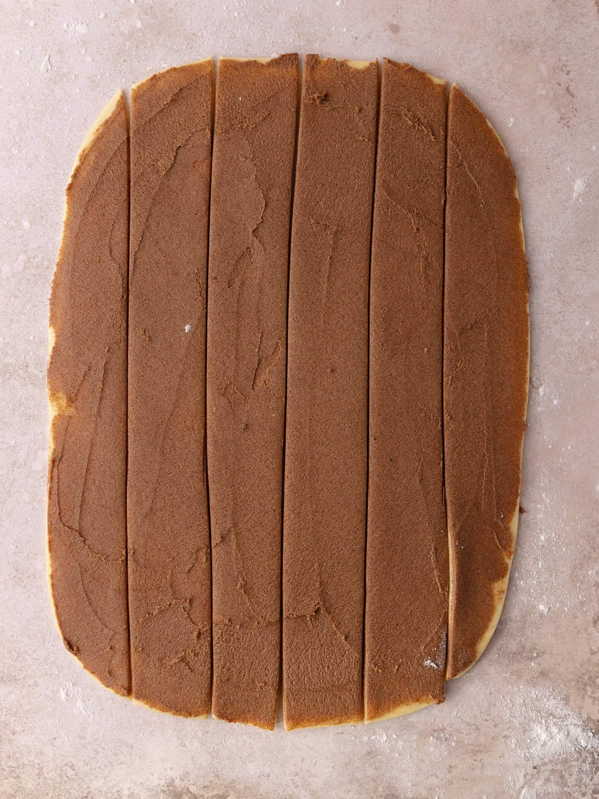 Cinnamon brown sugar filling is spread onto the dough and then cut into 6 2-inch wide strips.