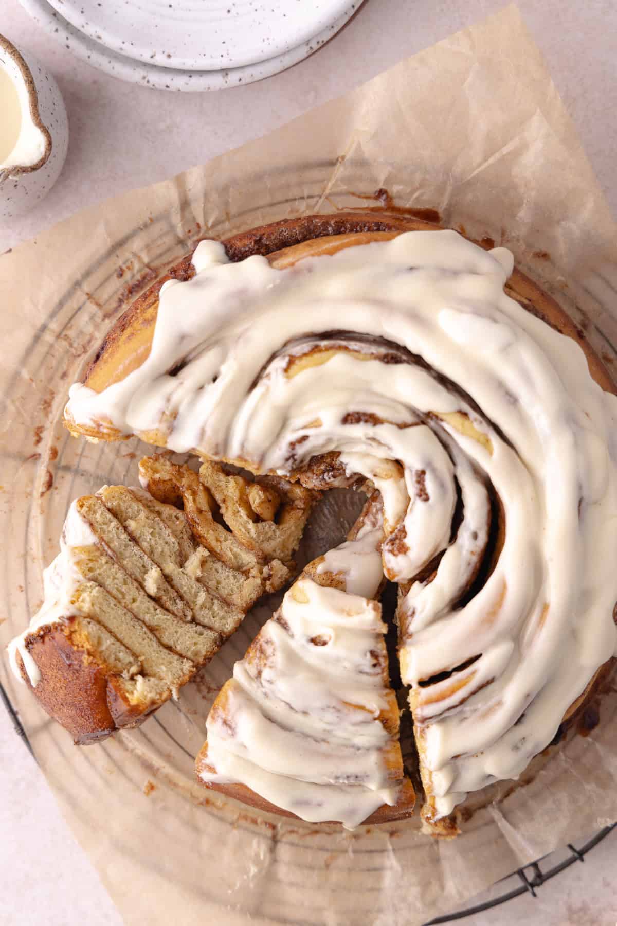 Giant cinnamon roll cake made with tangzhong milk bread brioche dough, sitting on a wire rack with slices cut.