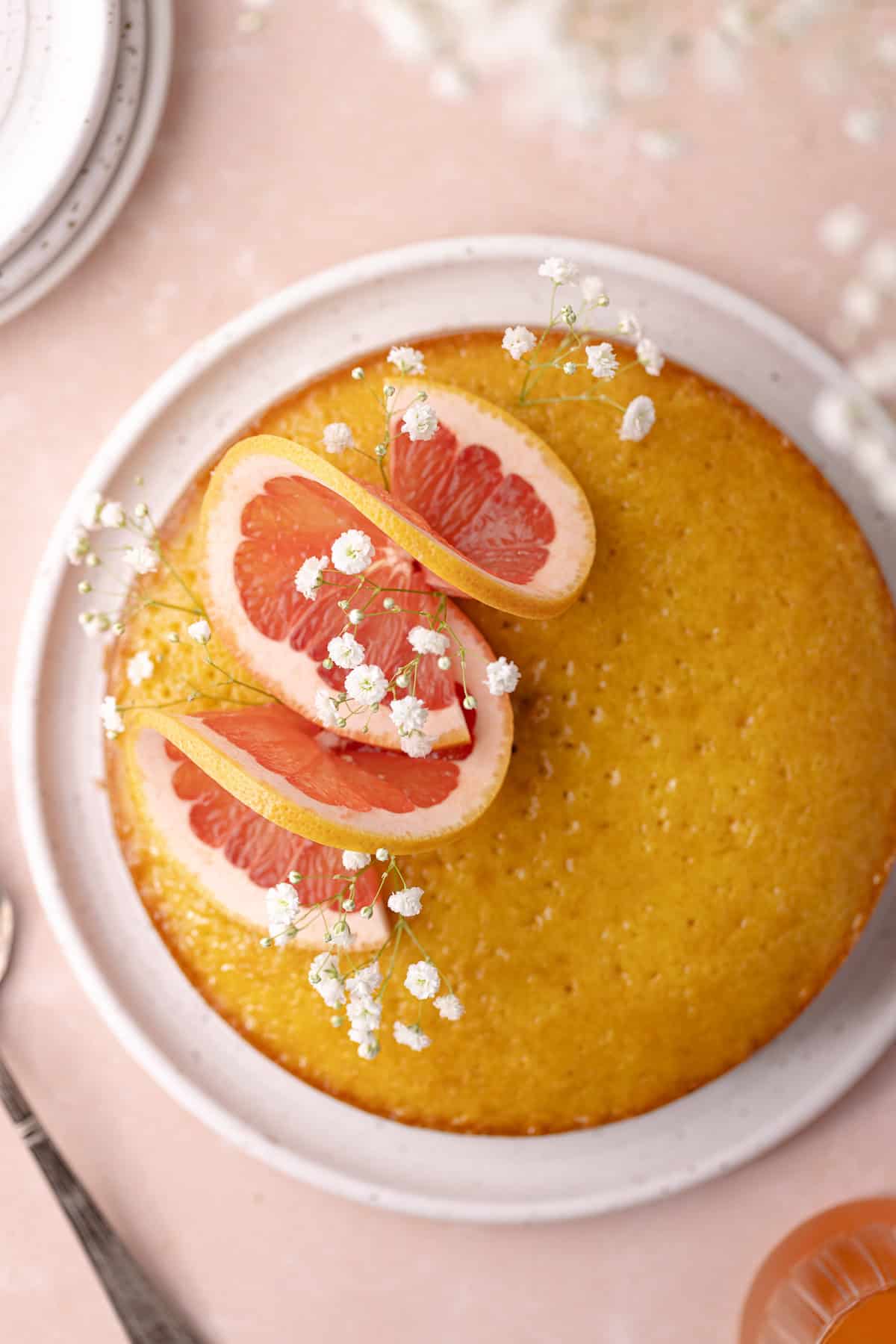 Soft and moist polenta grapefruit olive oil cake decorated with grapefruit slices and flowers.