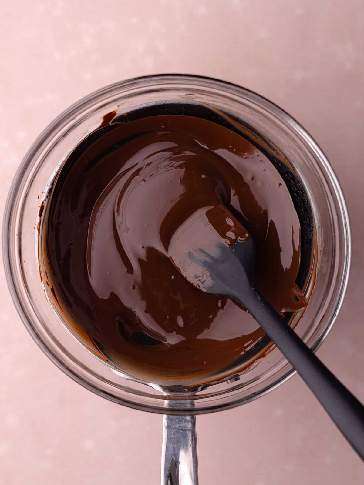 Chocolate is melted in a glass bowl sitting over a pot of simmering water.