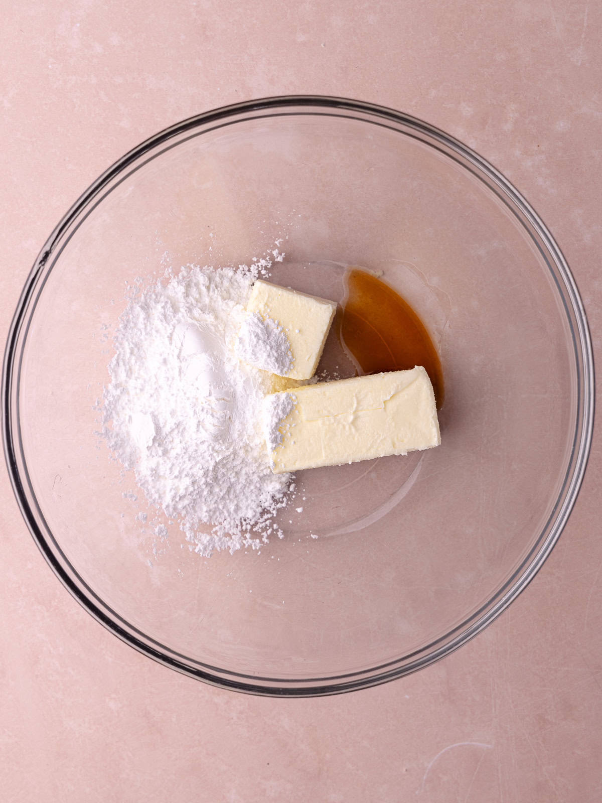 Very soft butter, powdered sugar and vanilla are sitting in a large glass mixing bowl.